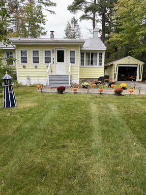 A yellow house with a garage, surrounded by a well-maintained lawn and various Halloween decorations. - On Caroga Time - Year Round Cottage With Private Dock (Caroga Lake)