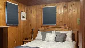 Un dormitorio con paneles de madera, una cama, dos mesitas de noche y un aplique de pared.