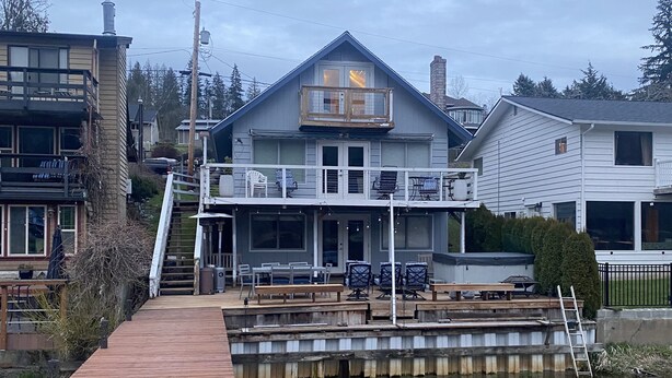 Una propiedad frente al mar con un muelle que lleva a una casa con balcón y mobiliario exterior.