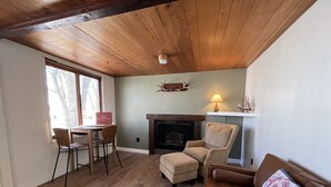 Een gezellige woonkamer met een open haard, een eethoek met een tafel en stoelen, en een bank met een decoratief kussen.