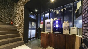 A reception area with a brick wall, a staircase, and a counter with a water dispenser and a vending machine.