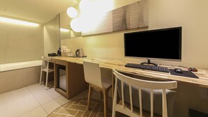 A modern bathroom with a shower, a toilet, and a sink with a mirror. There is a desk with a computer and a chair.