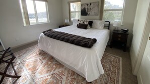 A bedroom with a large bed, a ceiling fan, two bedside tables with lamps, and a window with a view of the outdoors.