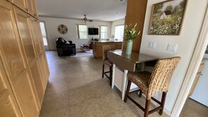A spacious kitchen with a dining area, a living room with a sofa, and a large window.