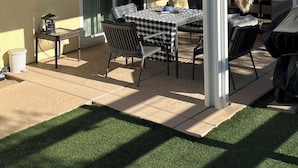 A covered patio with a table and chairs, a grill, and a sliding glass door leading to an interior space.