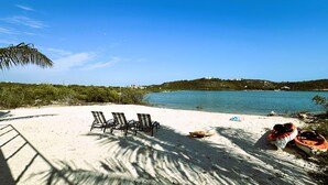 Una playa con tres tumbonas, un bote pequeño y una vista despejada del agua y colinas distantes.