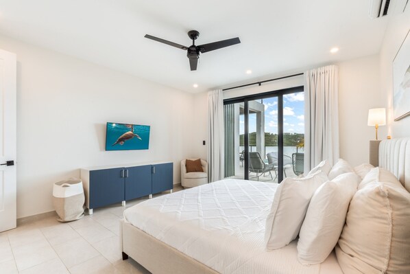 A bedroom with a bed, a ceiling fan, a view through a glass door, and a painting on the wall. - Márohu, 3BR Beach Oasis on Flamingo Lake (Venetian Road Settlement)