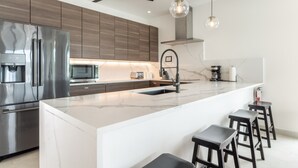 Una cocina moderna con una isla grande, electrodomésticos de acero inoxidable e iluminación colgante.
