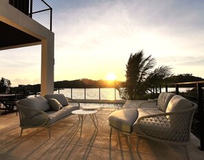An outdoor seating area with wicker furniture and a view of the sunset over water. - Márohu, 3BR Beach Oasis on Flamingo Lake (Venetian Road Settlement)