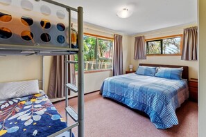 A bedroom with bunk beds, a bed, a window with curtains, and a view of greenery outside. - Games room, 250mtrs to beach, spacious, comfy beds (Baylys Beach)