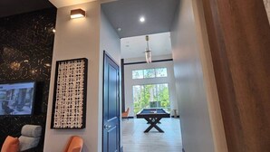 Un interior moderno con una mesa de billar, una zona de estar con sillas naranjas y un ventanal que ofrece vistas a la vegetación.