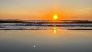 Una playa al atardecer con olas tranquilas y cielo despejado.