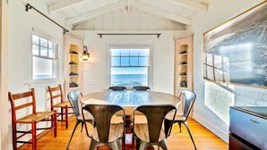 Un comedor con una mesa grande, sillas y vista al océano a través de una ventana.