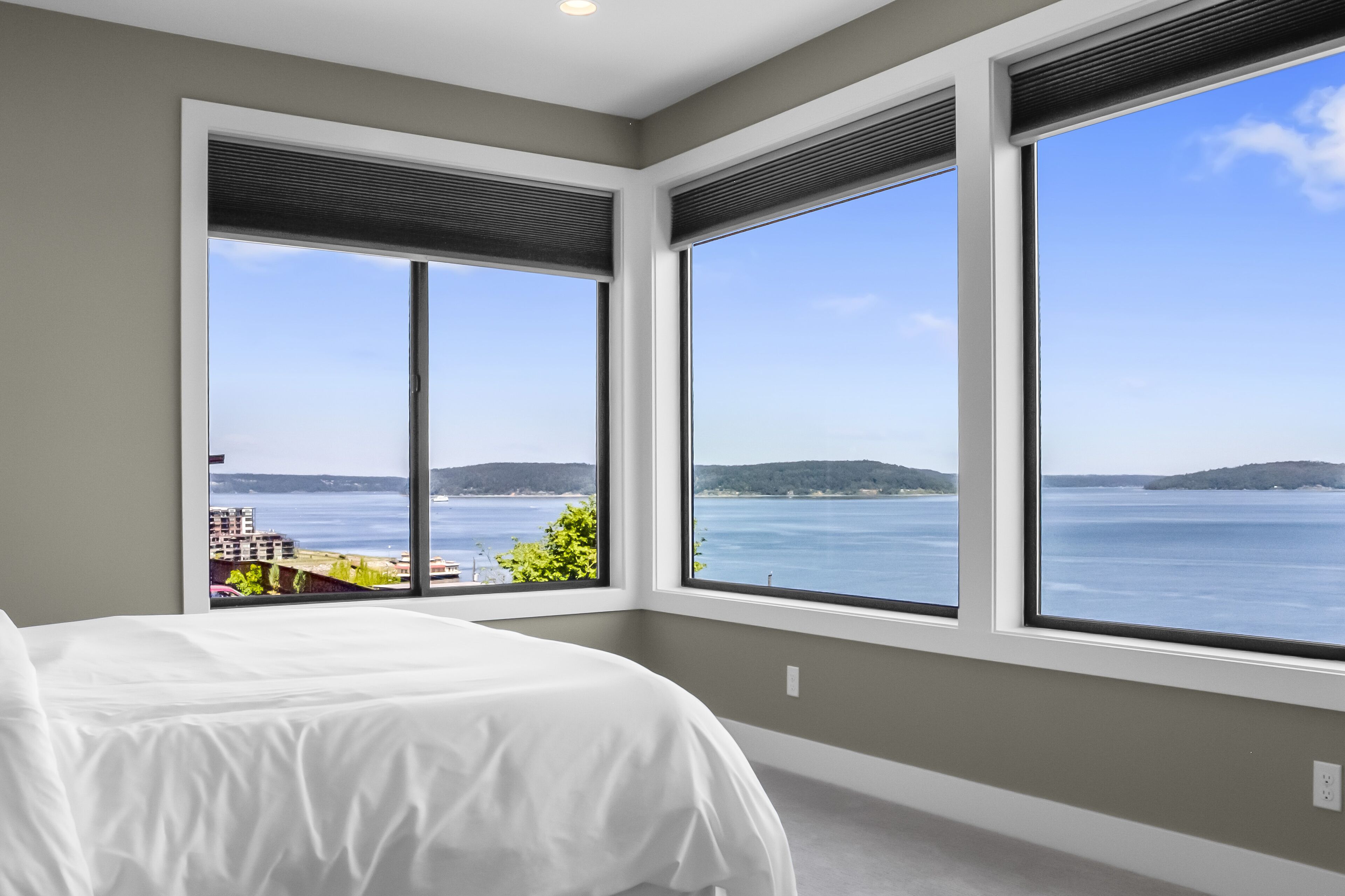 Une chambre à coucher avec un grand lit, trois fenêtres et une vue sur un plan d’eau.