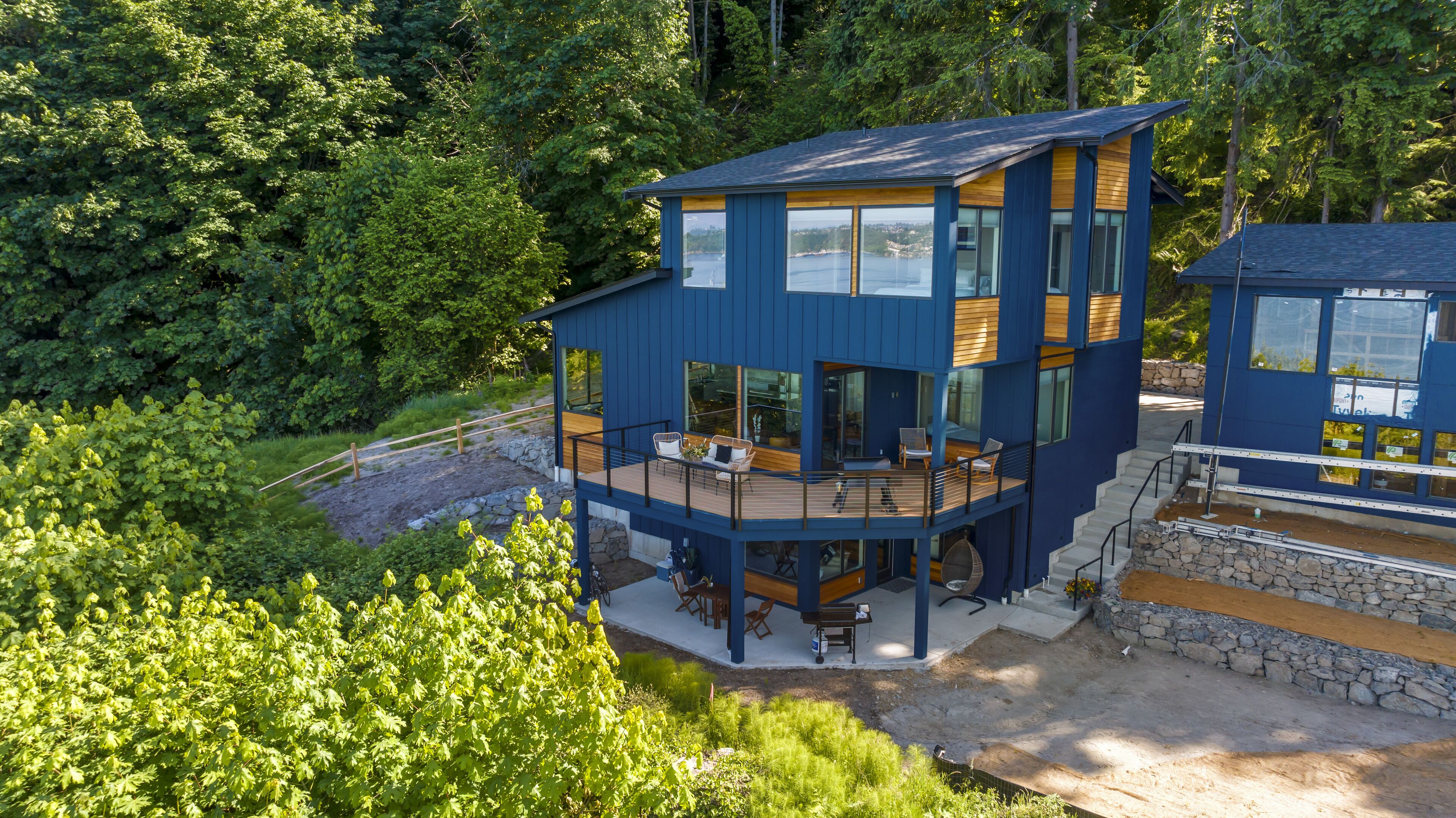 Une maison moderne à plusieurs niveaux, dotée d’une terrasse et entourée d’une forêt dense.