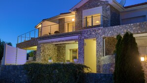 Una casa de piedra de dos pisos con balcón, antena parabólica y entrada protegida por portón.