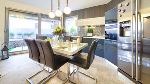 Una cocina moderna con una mesa de comedor de vidrio, sillas negras, electrodomésticos de acero inoxidable y vistas al exterior.