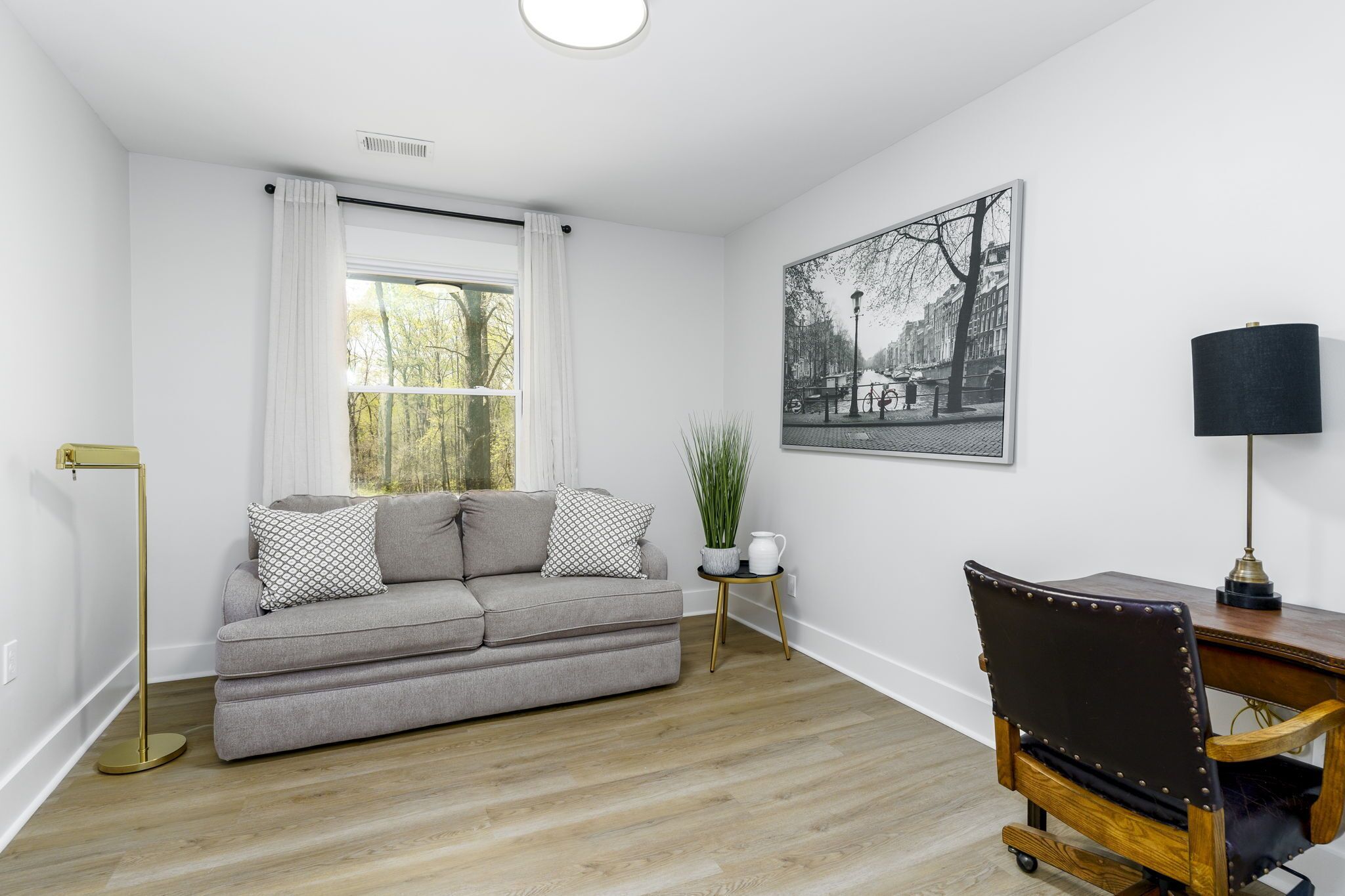 Un salon moderne avec un canapé gris, une petite table d’appoint ornée d’une plante, une lampe noire et une chaise en bois.