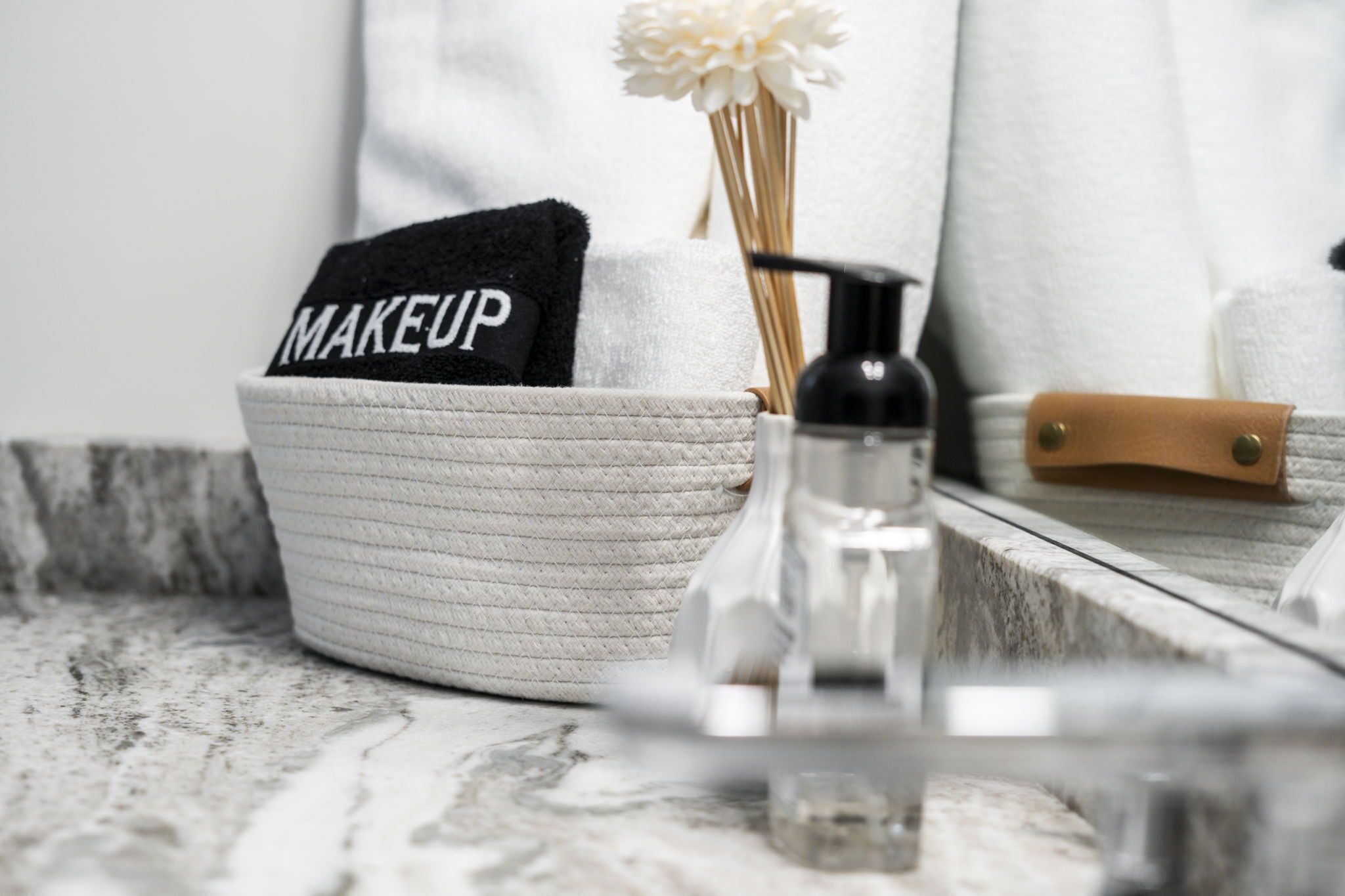 A bathroom with a white towel, a black towel with "MAKEUP" written on it, a bottle of soap, and a small container.