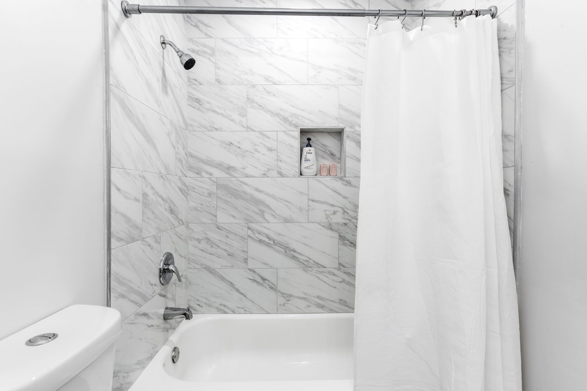 A bathroom with a shower, toilet, and a shelf with toiletries.