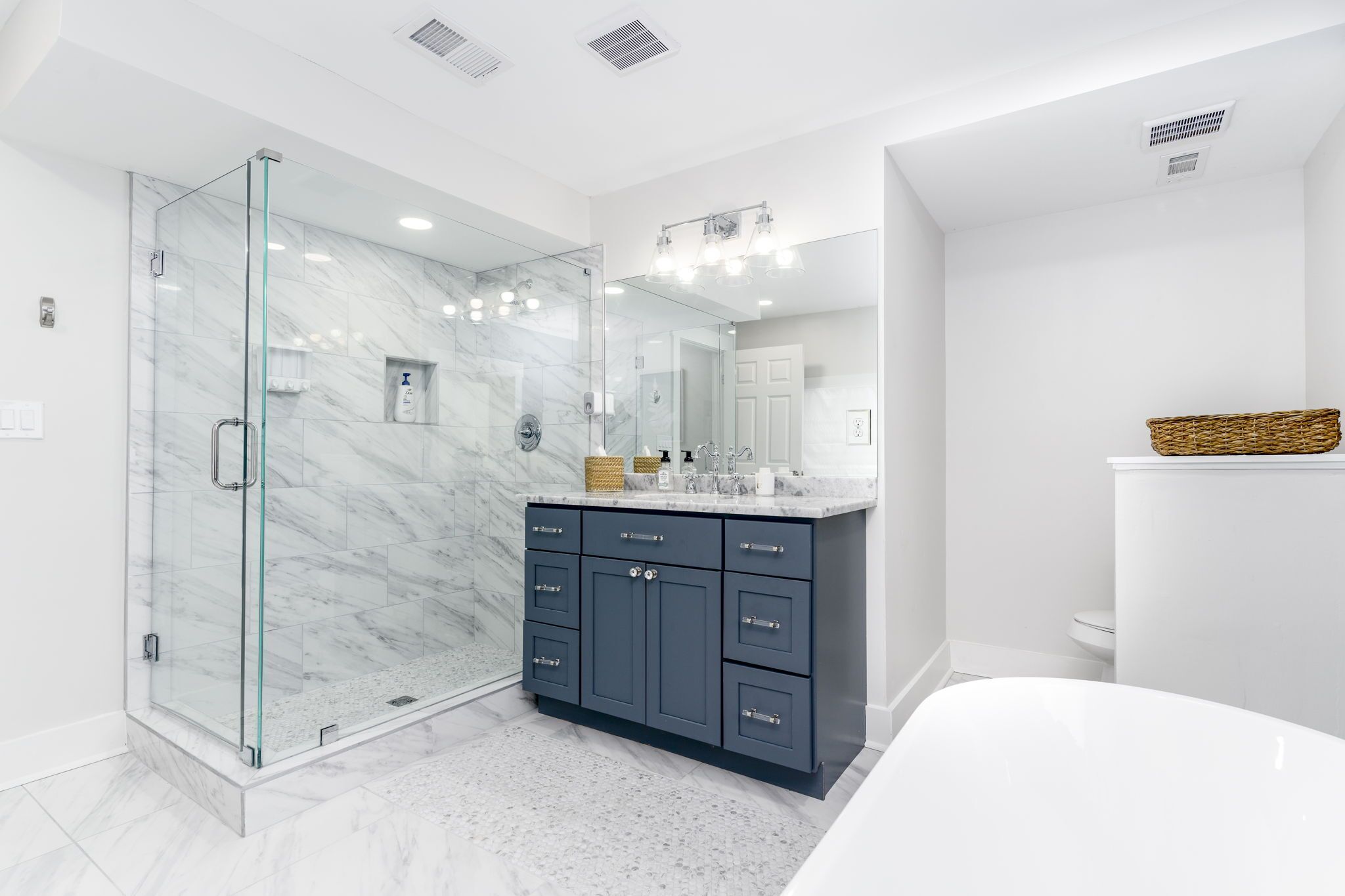 A modern bathroom with a glass-enclosed shower, a marble-tiled floor, a dark vanity with multiple drawers, and a large mirror above the sink.