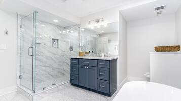 A modern bathroom with a glass-enclosed shower, a marble-tiled floor, a dark vanity with multiple drawers, and a large mirror above the sink.