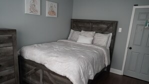 Un dormitorio con estructura de cama de madera, ropa de cama blanca y dos cuadros en la pared.
