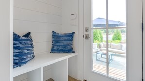 A white bench with two blue patterned cushions, a white door, and a view of an outdoor seating area with a table and chairs. - New Construction! 5 bedroom home with community clubhouse and pool (Nantucket)