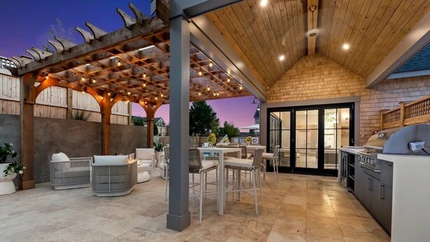 A covered outdoor kitchen area with a pergola, seating, and a view of the house. - New Construction! 5 bedroom home with community clubhouse and pool (Nantucket)