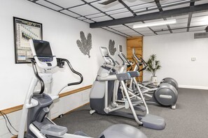 Un gimnasio con varias cintas de correr, elípticas y una bicicleta estática.