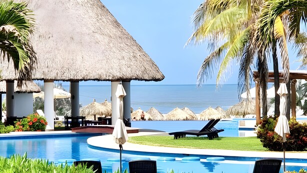 A pool area with lounge chairs, a thatched-roof structure, and a view of the ocean. - Luxury Diamante Apartment, Private Beach Club, 4 Bedrooms, 8 Guests (Acapulco de Juárez)