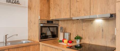 A kitchen with wooden cabinets, a stainless steel oven, a sink, and a countertop with vegetables.