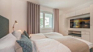 Una habitación de hotel con cama, escritorio, televisor y ventana con cortinas.
