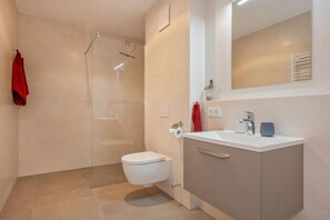 Ein modernes Badezimmer mit Duschkabine aus Glas, Toilette, Waschbecken mit Spiegel und Handtuchhalter.