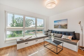 Ein modernes Wohnzimmer mit großem Fenster, einer Couch, einem Couchtisch und einem Gemälde an der Wand.