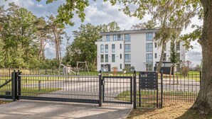 Una entrada cerrada a un edificio residencial con un camino de entrada pavimentado y un parque infantil al fondo.
