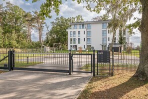 A gated entrance to a residential building with a paved driveway and a playground in the background.