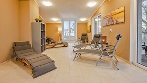 A sunroom with reclining chairs, a massage table, and a large window providing a view of the outdoors. - Ferienwohnung Terrasse am Haff - Hochwertig Eingerichtetes Ferienappartment in Ruhiger Lage mit Wlan (Zirchow)