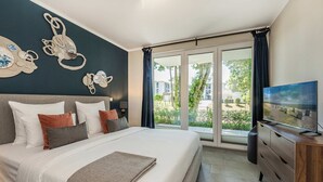Une chambre moderne avec un grand lit, une télévision et une vue sur un jardin, accessible par une porte coulissante.