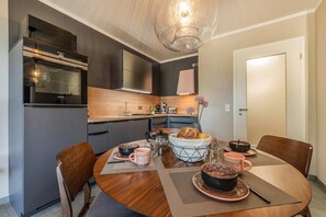 A modern kitchen with a dining table set for four, featuring a central island with a bowl of bread and a vase of flowers. - Ferienwohnung Terrasse am Haff - Hochwertig Eingerichtetes Ferienappartment in Ruhiger Lage mit Wlan (Zirchow)