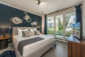 A modern bedroom with a large bed, a flat-screen TV, and a view of the outdoors.