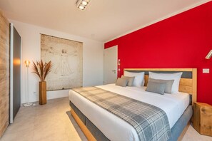 A modern bedroom with a large bed, a red accent wall, and a large framed artwork on the wall. - Ferienwohnung Ein Traum am Haff - Hochwertiges Ferienapartment in Ruhiger Süd-west Lage mit Sauna, (Zirchow)