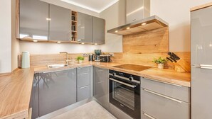 A modern kitchen with grey cabinets, a built-in oven, a coffee machine, and a stainless steel refrigerator. - Ferienwohnung Ein Traum am Haff - Hochwertiges Ferienapartment in Ruhiger Süd-west Lage mit Sauna, (Zirchow)