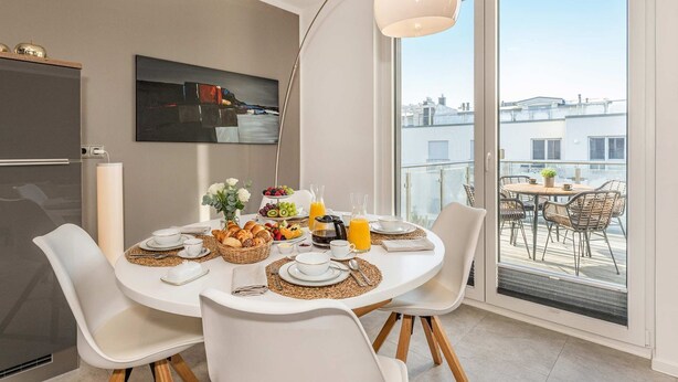 A dining area with a table set for breakfast, a large window with a city view, and a modern pendant light. - Ferienwohnung Ein Traum am Haff - Hochwertiges Ferienapartment in Ruhiger Süd-west Lage mit Sauna, (Zirchow)