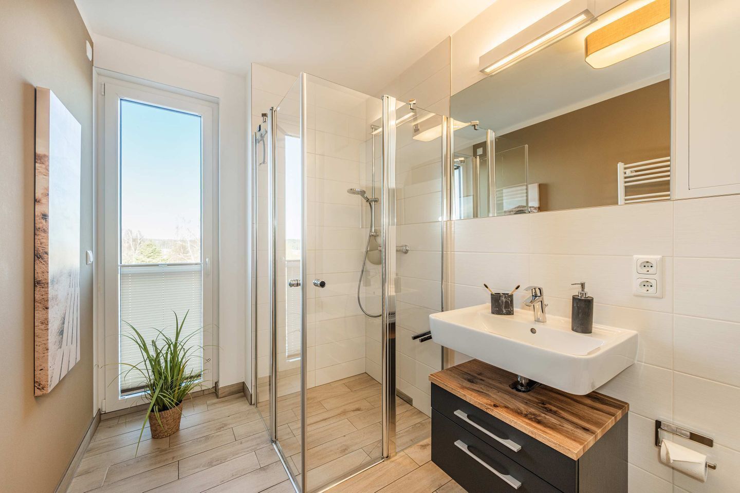 Un baño moderno con cabina de ducha de vidrio, un lavamanos blanco con encimera de madera y un espejo grande.