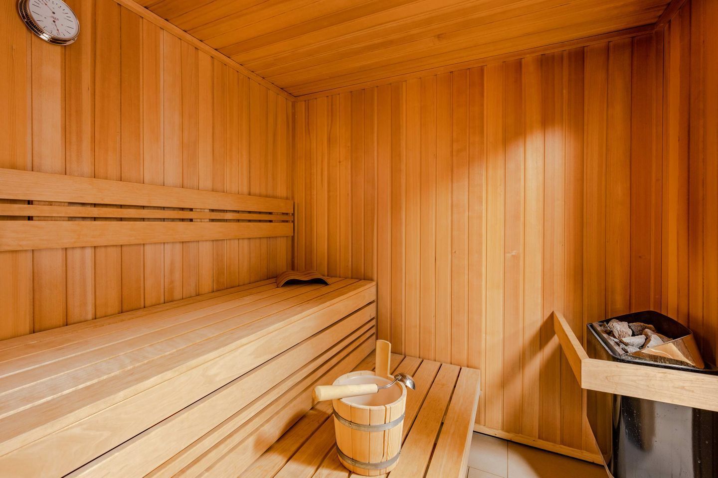 A sauna with wooden benches, a wooden bucket, and a metal container.