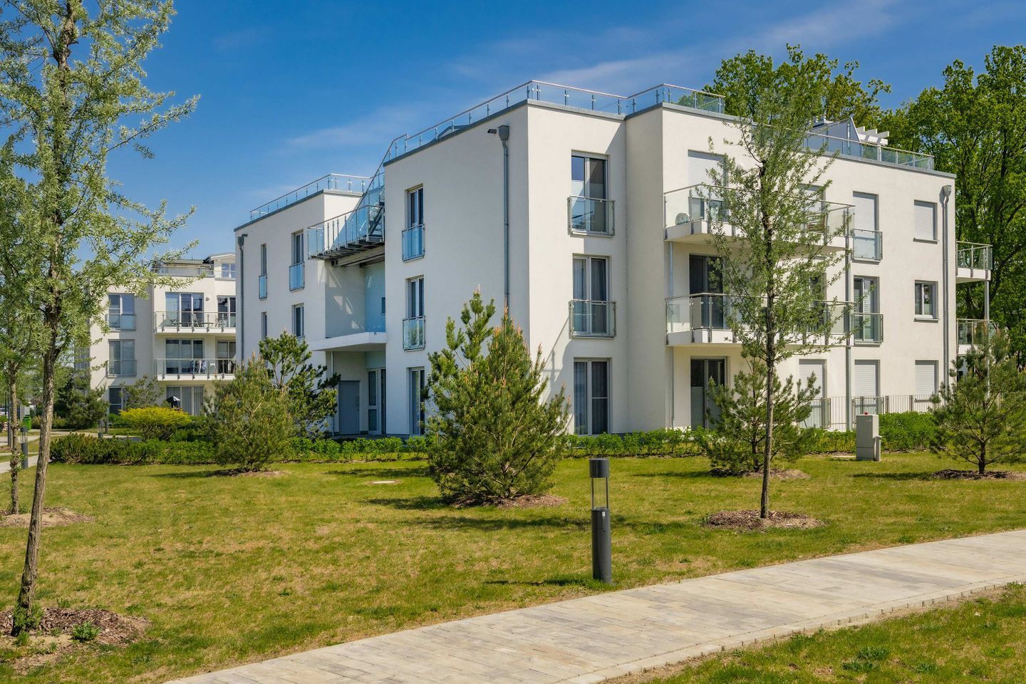 Un immeuble d’appartements moderne doté de nombreux balcons, d’une pelouse bien entretenue et surplombant un ciel dégagé.