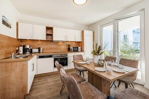 A modern kitchen with white cabinets, a wooden countertop, and a dining area with a wooden table and chairs. - Ferienwohnung Klippenblick (Garz)