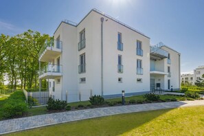 A multi-story residential building with balconies, a paved driveway, and a well-maintained lawn. - Ferienwohnung Klippenblick (Garz)