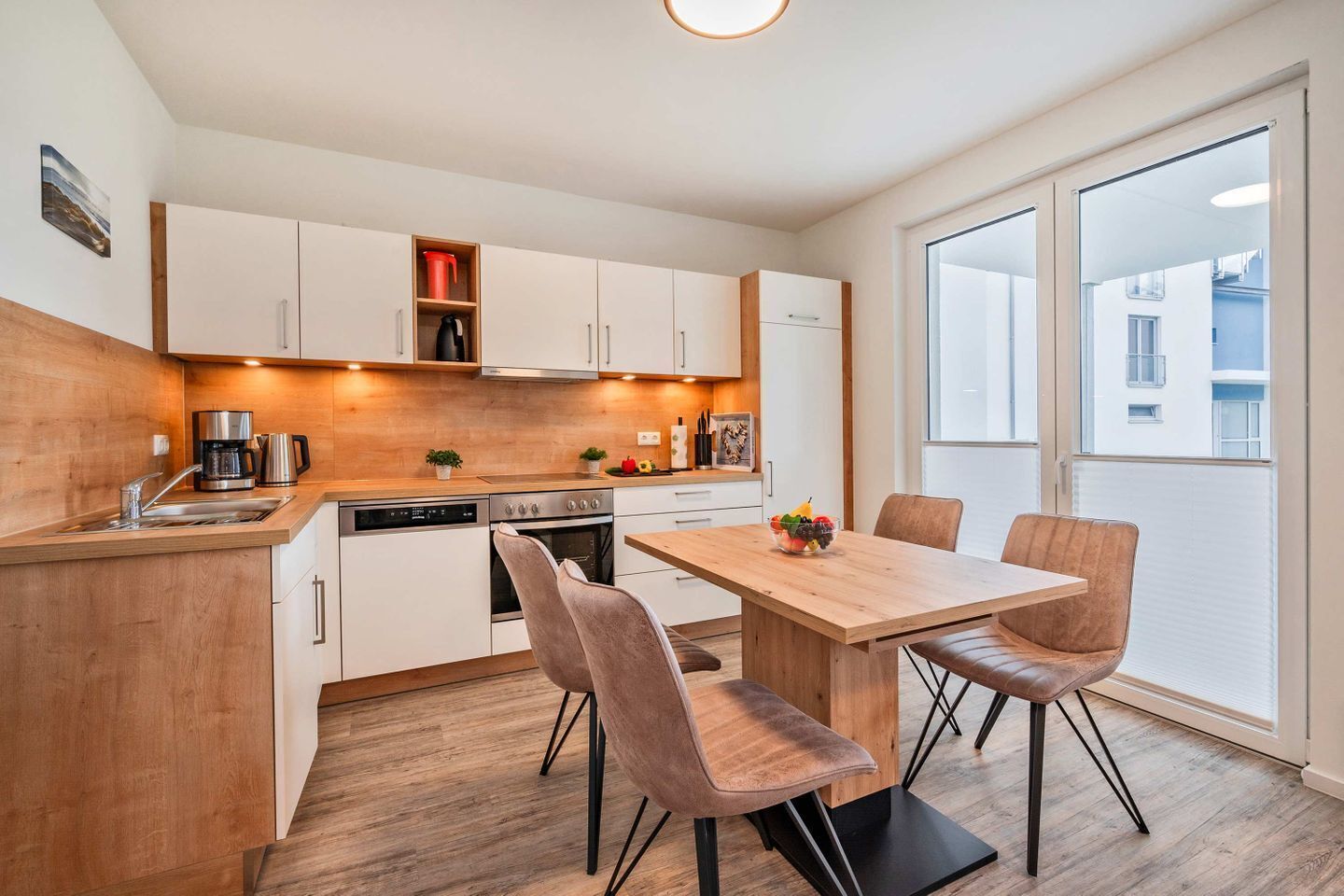 Una cucina moderna con mobili bianchi, un piano di lavoro in legno e un'area pranzo con tavolo e sedie.